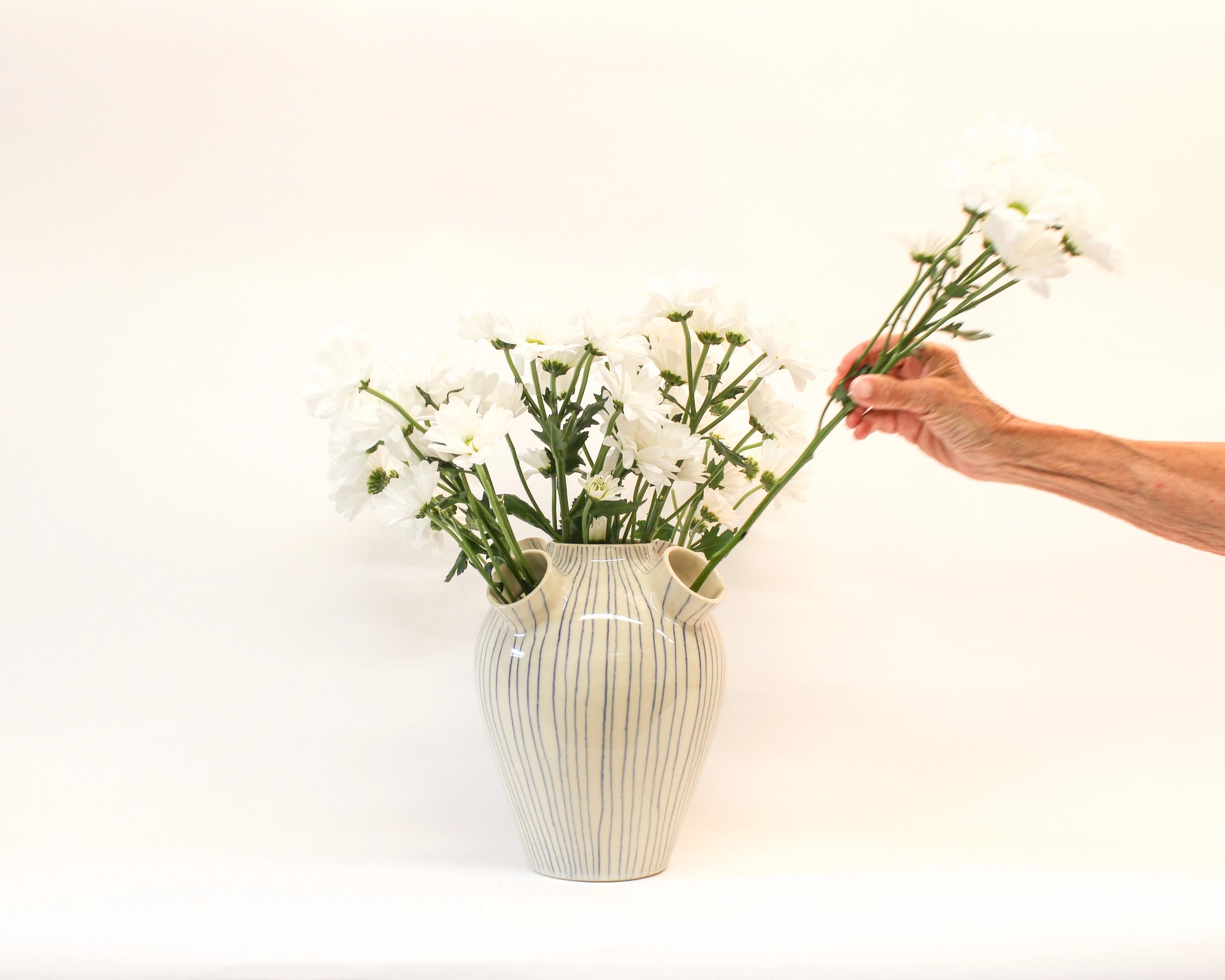 Person arranging flowers into a handmade wheel thrown white ceramic vase with blue stripes from Mima Ceramics by Michelle Organ.