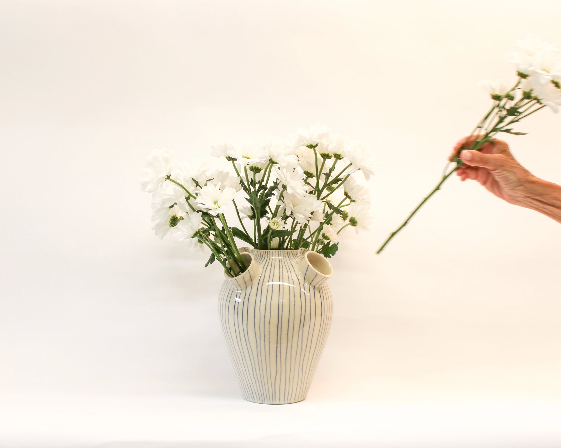 Person arranging flowers into a white handmade ceramics vase  with blue stripes from Mima Ceramics by Michelle Organ. 