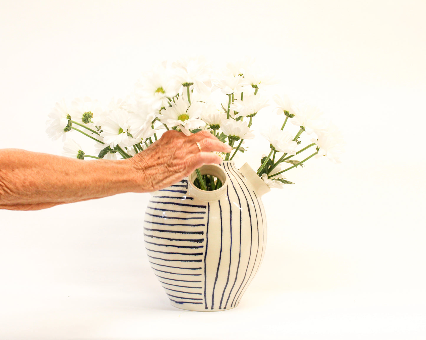 Person arranging flowers into a handmade ceramic striped vase on a white background from Mima Ceramics by Michelle Organ. 