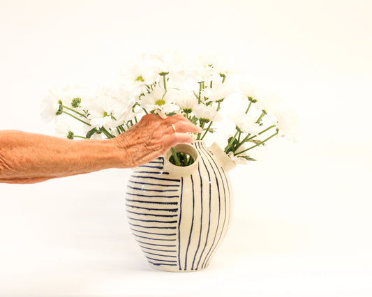Person arranging flowers into a handmade ceramic striped vase on a white background from Mima Ceramics by Michelle Organ. 