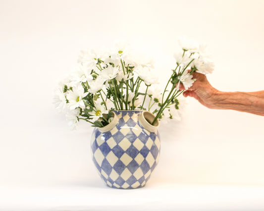 Hand arranging flowers into a handmade ceramic blue and white harlequin vase on a white background from Mima Ceramics by Michelle Organ.  