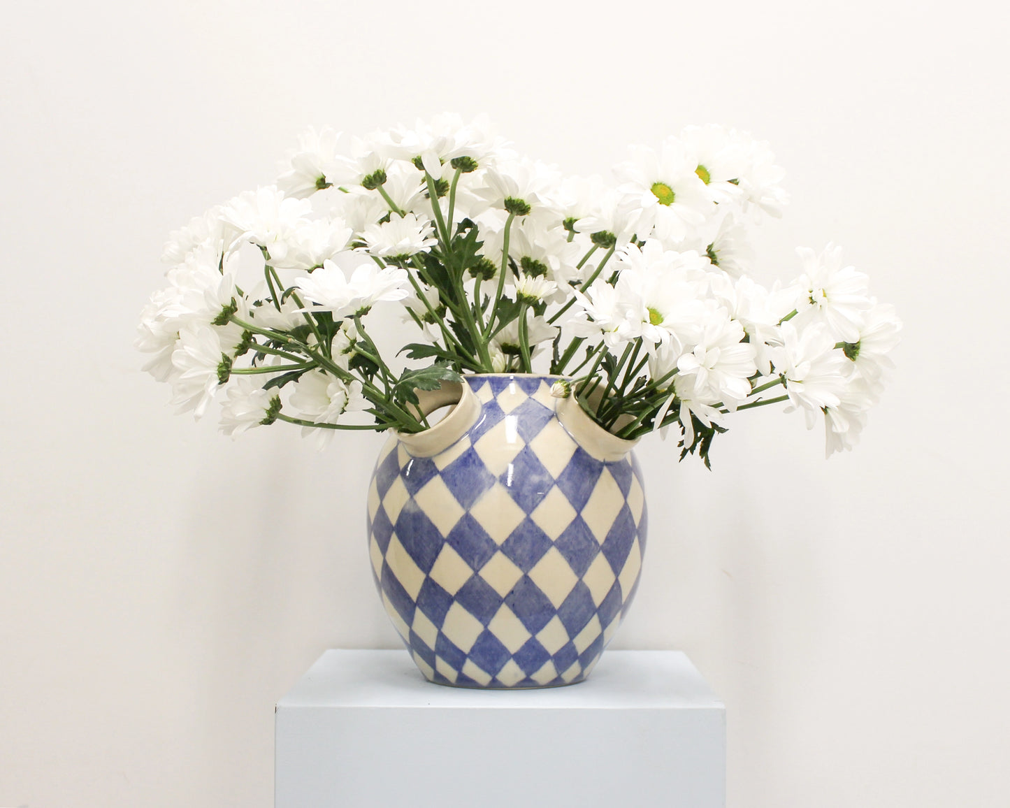 Blue and white checkered vase with white flowers on a light background from Mima Ceramics by Michelle Organ.