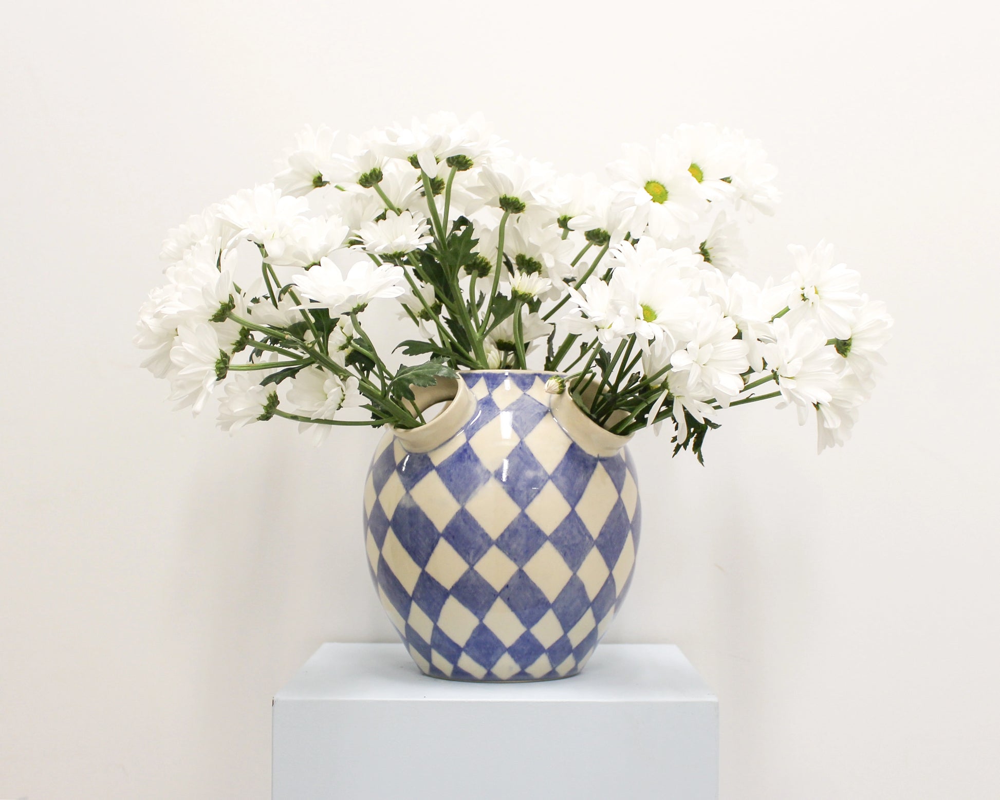 Blue and white checkered vase with white flowers on a light background from Mima Ceramics by Michelle Organ.
