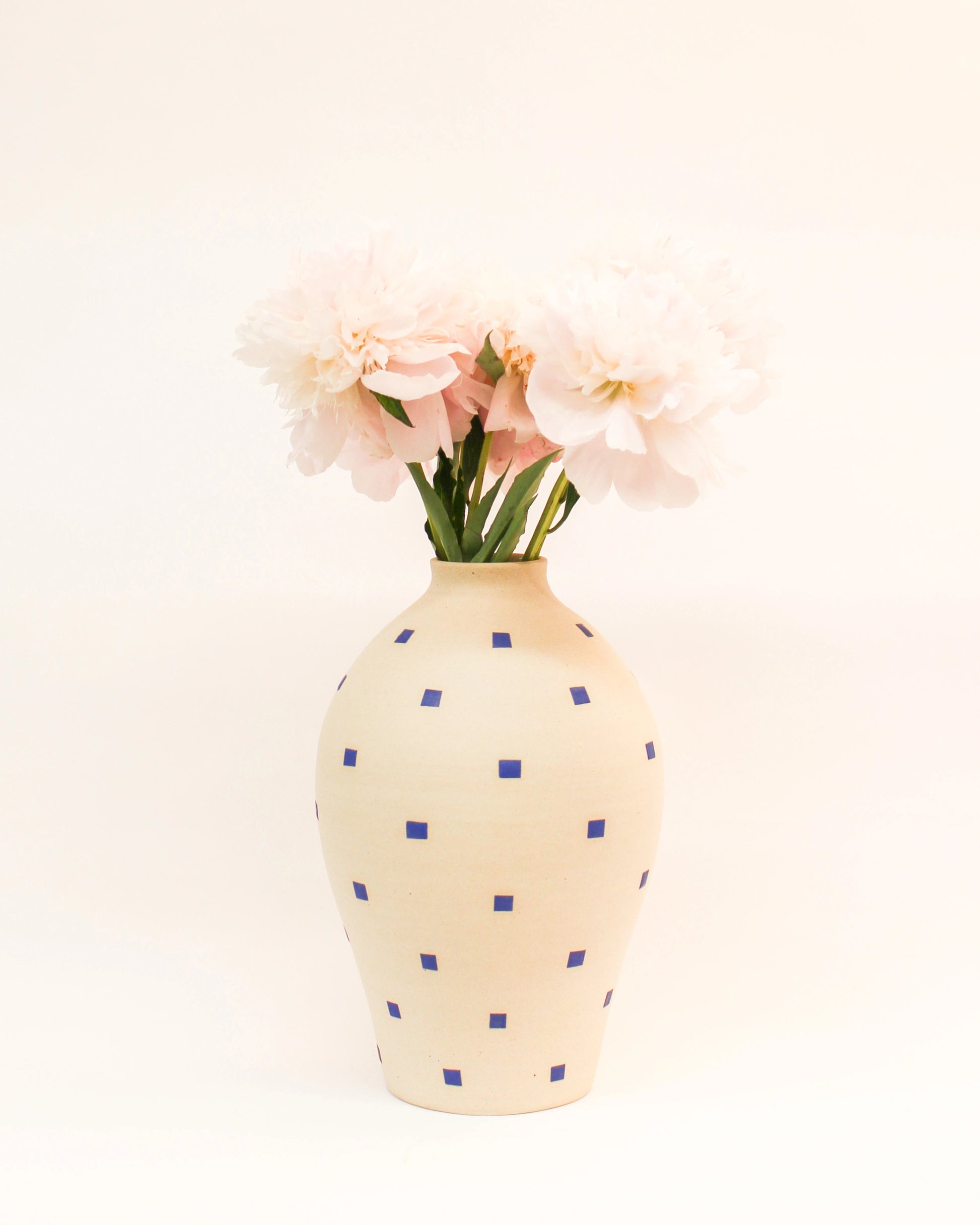 Handmade Cream-colored vase with blue polka dots holding pink flowers on a white background from Mima Ceramics by Michelle Organ.