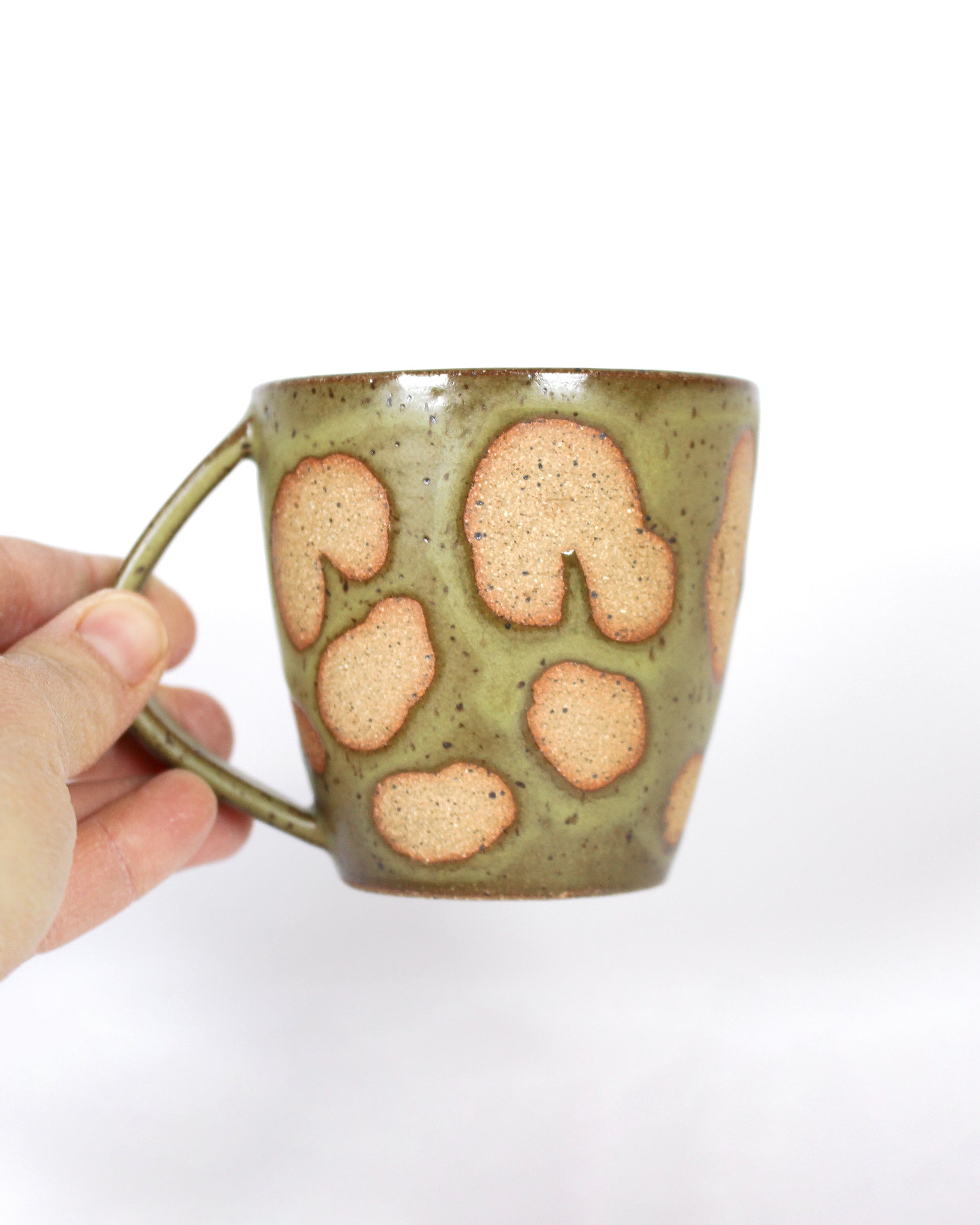 Hand holding a ceramic mug with brown and green speckled design 