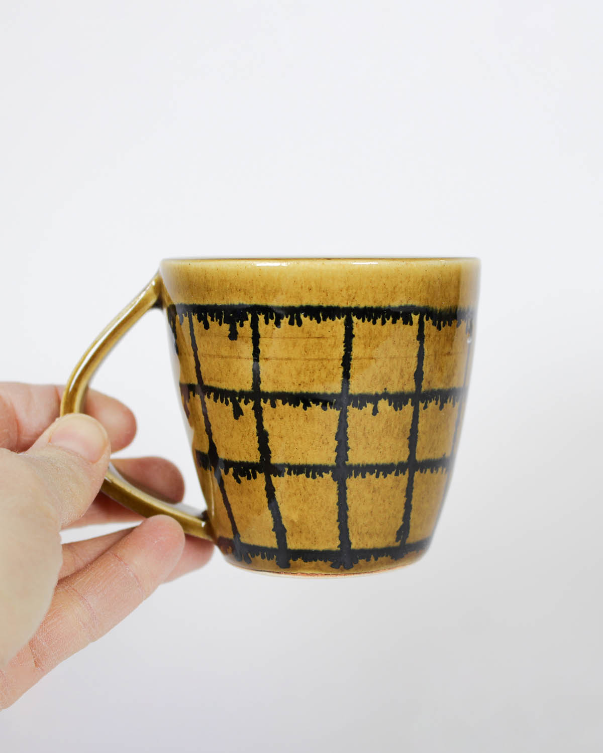 Hand holding a butterscotch mug with black grid pattern, made in Toronto. 